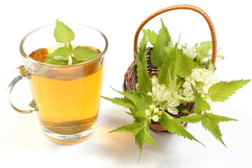 Fresh nettle in wicker basket and cup of beverage
