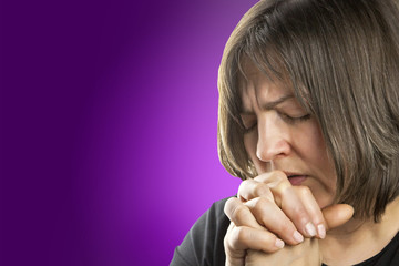 Mature woman in fervent prayer on violet background © hriana