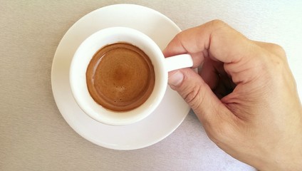 Small white cup of strong black espresso coffee and male hand