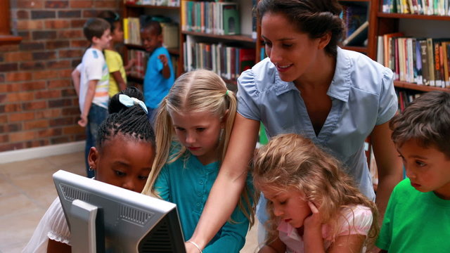 Pupils looking at the computer in library with their teacher