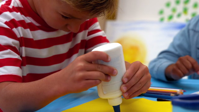 Cute little boy using glue in classroom