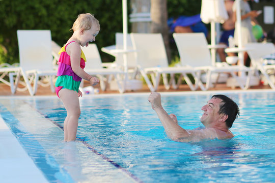 Father and daughter having fun in outdoors swimming pool