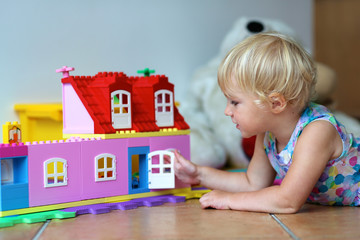 Happy preschooler girl building house from plastic blocks