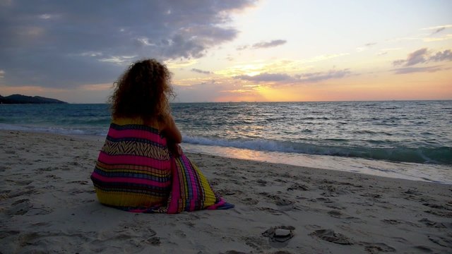 Worried Sad Girl Sitting on the Beach at Sunset. Slow Motion.
