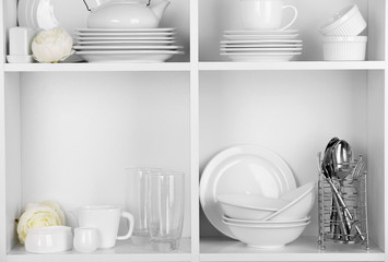 Different white clean dishes on wooden shelves