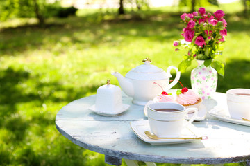 Coffee table with teacups and tasty cakes in garden