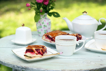 Coffee table with teacups and tasty pie in garden