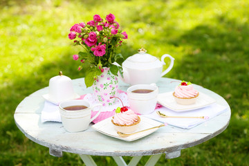 Coffee table with teacups and tasty cakes in garden