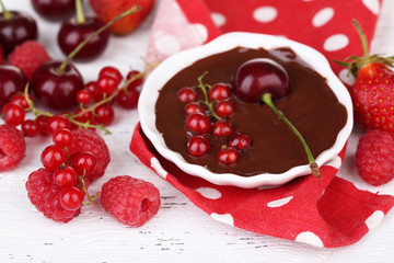 Ripe sweet berries and liquid chocolate on wooden table