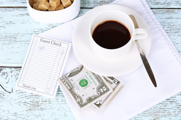 Check, money and cup of coffee on table close-up