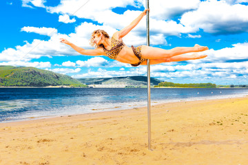 girl make pole dance in a swimsuit on the beach background sky