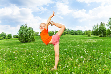 Beautiful little girl doing gymnastics on a grass