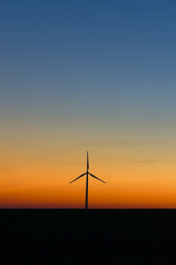 Silhouette of wind turbine generating electricity on sunset.