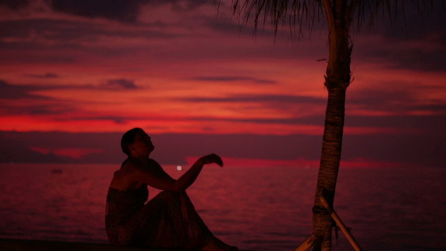 Woman sitting alone in the darkness at seashore, steadycam shot