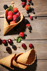 Different ripe berries in sugar cone, on wooden background