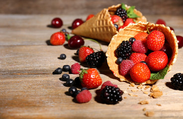 Different ripe berries in sugar cones, on wooden background