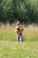 Little pretty girl stands on green grass and holds camera