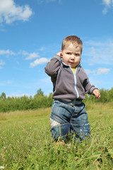 Little handsome boy stands at green meadow and thinks