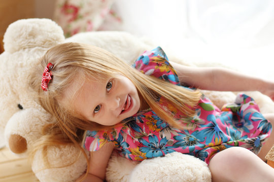 Pretty little girl lies on big soft toy bear and looks at camera