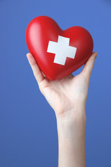 Red heart with cross sign in female hand, close-up,