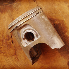Damaged piston with intake valve on a white wooden table