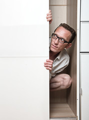 Prying man hiding inside white wardrobe  Copy space left
