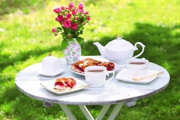 Coffee table with teacups and tasty pie in garden