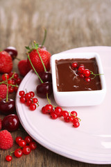 Ripe sweet berries and liquid chocolate on wooden table