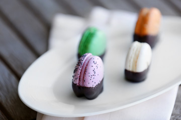 Colorful macaroons in plate on wooden table, close-up
