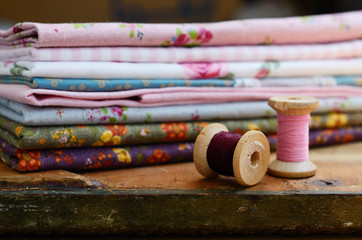Wooden thread spools and floral pattern fabric set - obrazy, fototapety, plakaty
