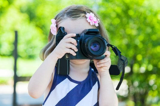 Little girl who takes pictures with a photo camera in park