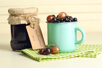 Ripe blackcurrants in mug and glass jar with tasty jam