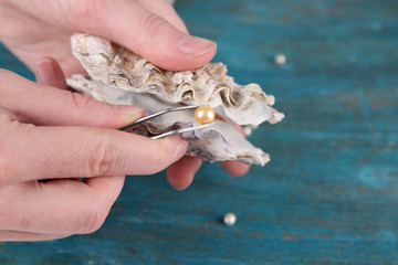 Hand with tweezers holding pearl and oyster on wooden