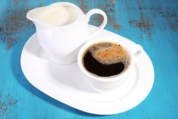 Cup of coffee, creamer on color wooden background
