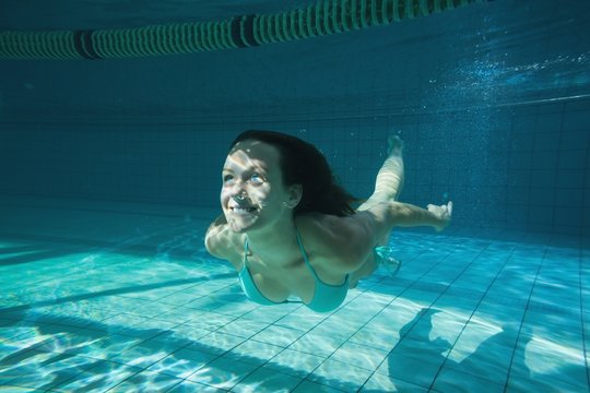 Pretty brunette smiling and swimming underwater