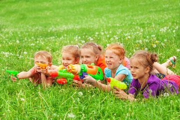 Fototapeta premium Kids play with water guns laying on a meadow