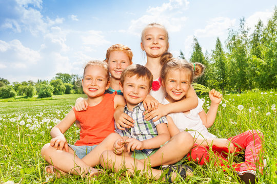 Five wonderful kids sitting together on a meadow