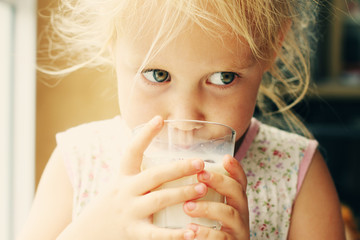 Cute cheerful little girl drinking milk