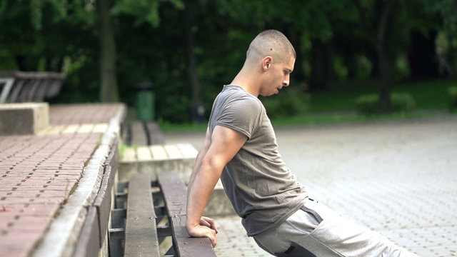 Young man doing push-ups on bench in park, super slow motion