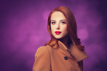 Redhead women in coat on vilolet background.