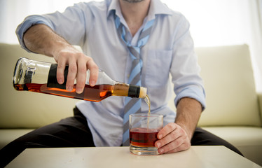 nk Businessman filling whiskey glass sitting on couch at home