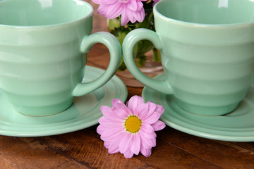 Cups and saucers with flowers on wooden background