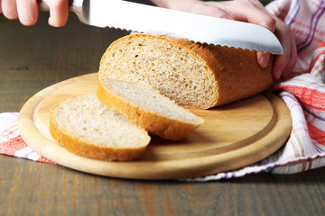 Female hands cutting bread on wooden board, close-up