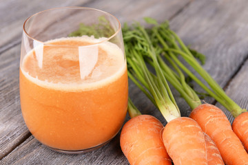 Glass of carrot juice and fresh carrots on wooden background