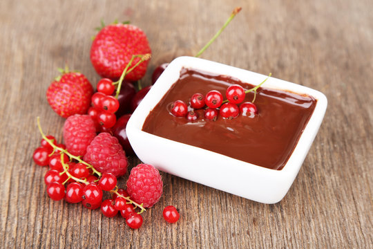 Ripe sweet berries and liquid chocolate on wooden table