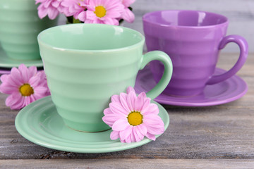 Cups and saucers with flowers on wooden background