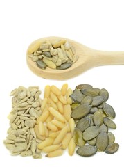 Piles of pine nuts, sunflower, pumpkin seeds with wooden spoon