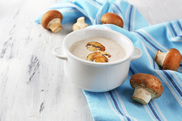 Mushroom soup in white pot, on napkin,  on wooden background
