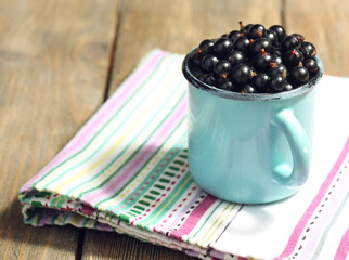 Ripe blackcurrants in mug on wooden background.