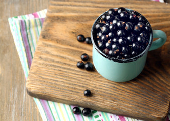 Ripe blackcurrants in mug on board, on wooden background.